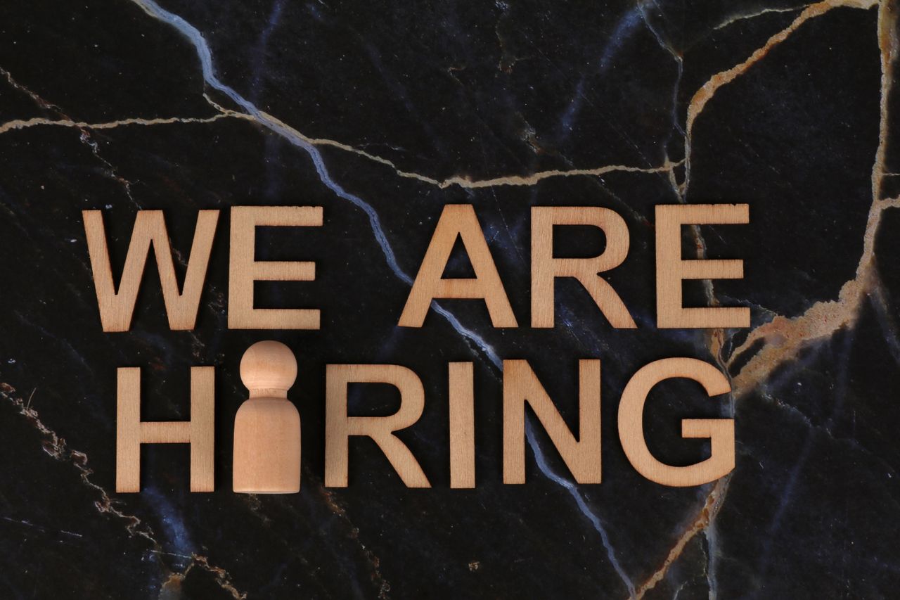 heros-img Wooden letters spell 'We Are Hiring' on dark marble surface.