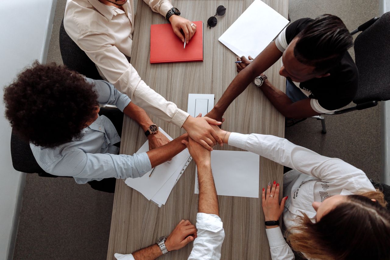 The Art of Drawing Readers In: Your attractive post title goes here Overhead view of a diverse team placing hands together in a sign of unity during a meeting.